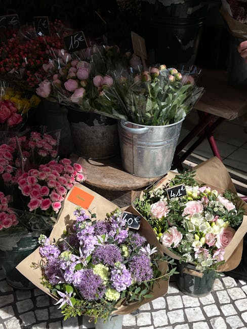 A vibrant display of fresh flower bouquets arranged on a rustic wooden table outside a floristry shop. The assortment includes a bouquet of purple and white flowers with lavender and green foliage wra